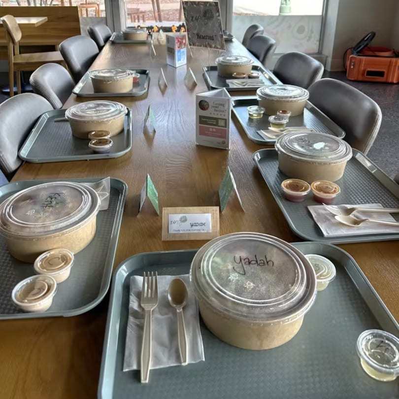 A long wooden table set with multiple individual Up Leaf Café Asian takeout meals on trays.