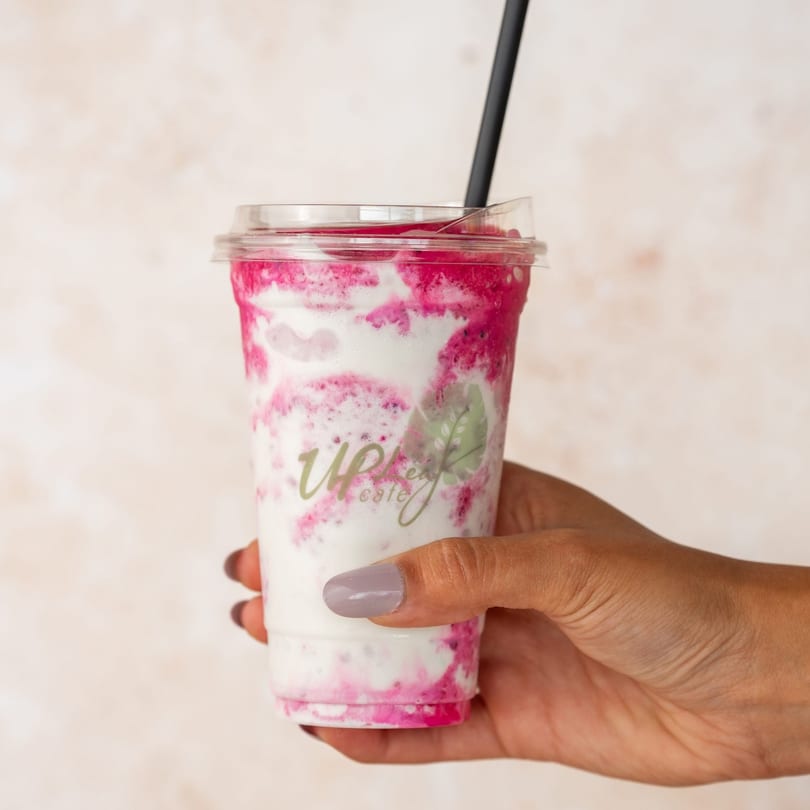 Hand holding a clear plastic cup of Up Leaf Café's pink and white swirled drink with a black straw.
