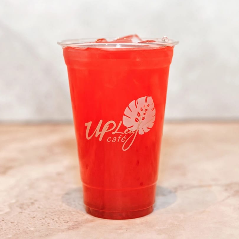 A vibrant red iced drink in a clear plastic cup with the Up Leaf Café logo.