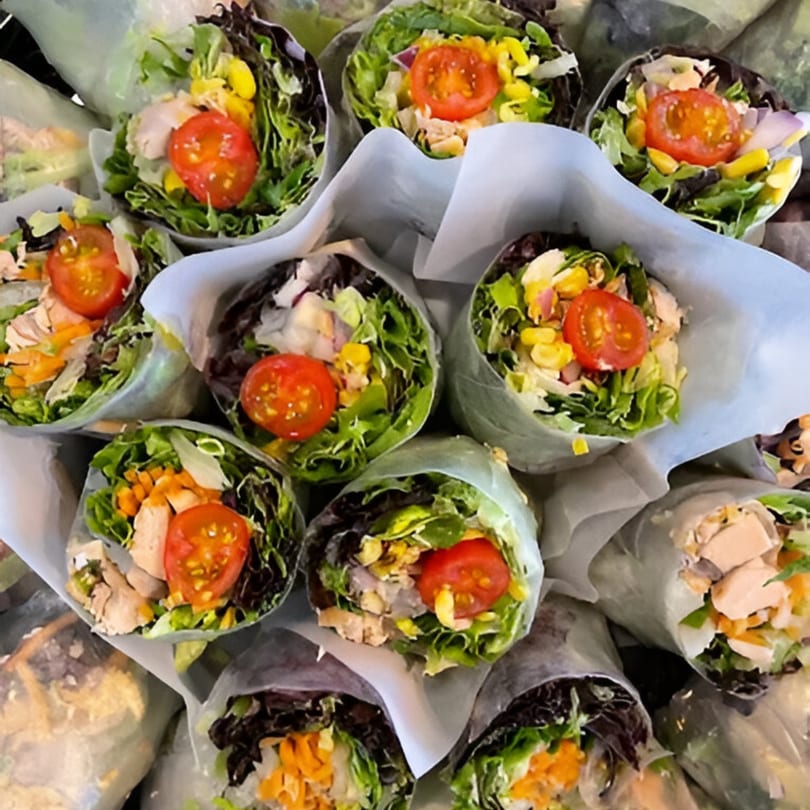 Close-up of numerous fresh Up Leaf Café spring rolls with lettuce, chicken, corn, and tomatoes.