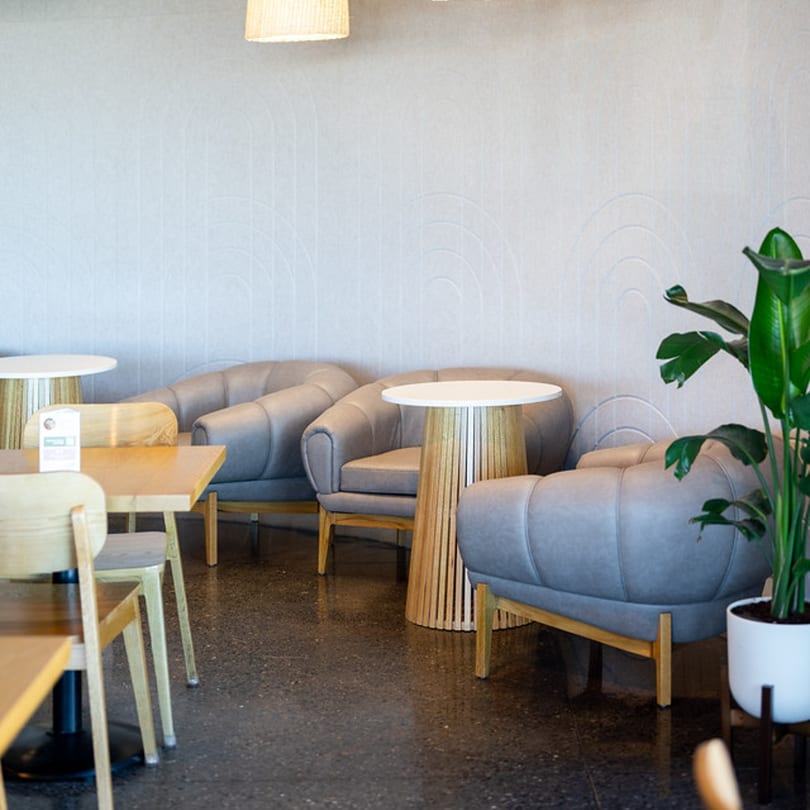 Up Leaf Café's interior features gray armchairs, light wood tables, and a potted plant on a dark floor.