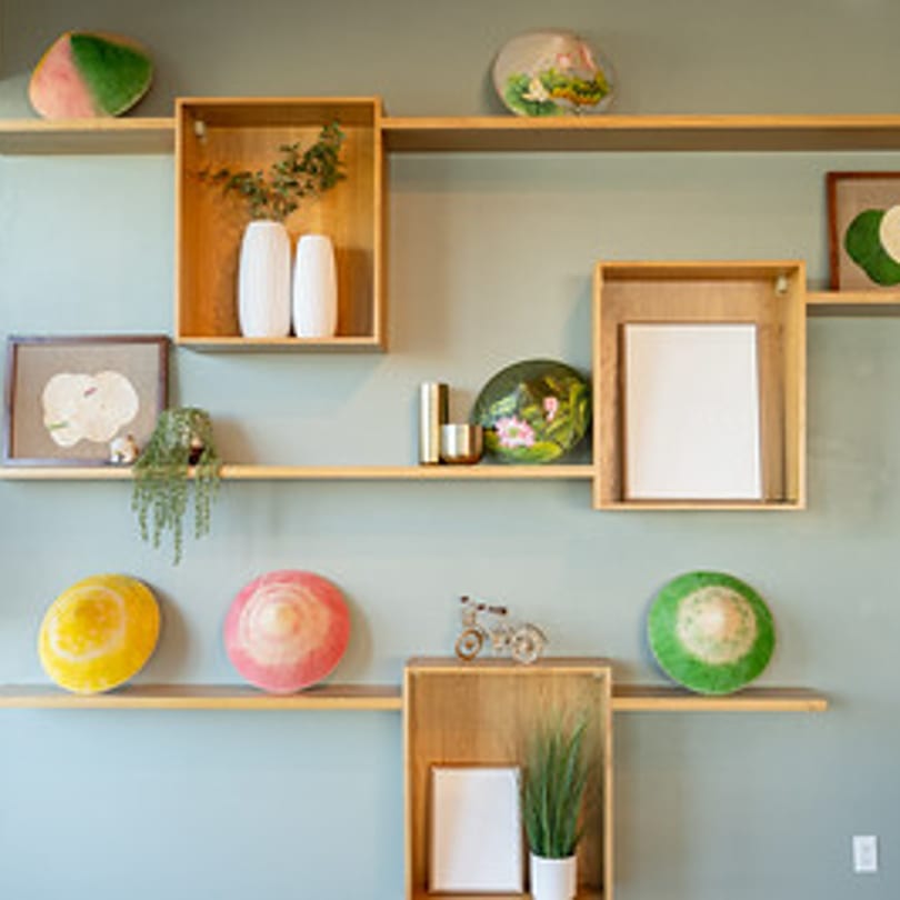 Wall decor at Up Leaf Café featuring wooden shelves with vases, plants, and colorful Asian-inspired art.