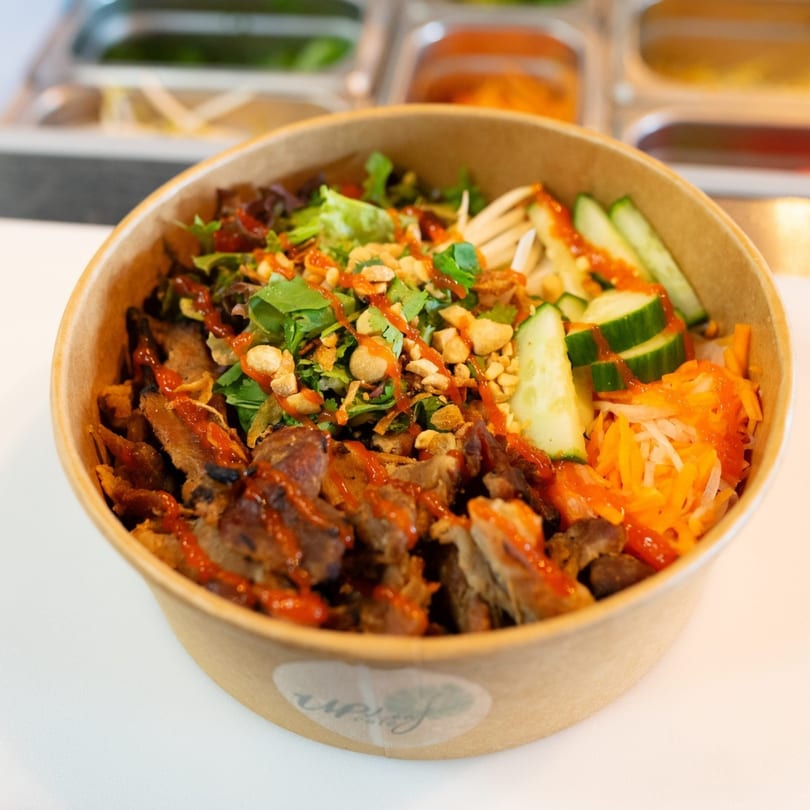 Up Leaf Café's Asian bowl with meat, vegetables, peanuts, and chili sauce in a brown paper bowl.